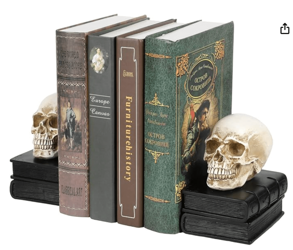 A set of spooky bookends showing two realistic aged-beige skulls resting on small decorative black books, securely holding a row of vintage-style hardcover books in place.