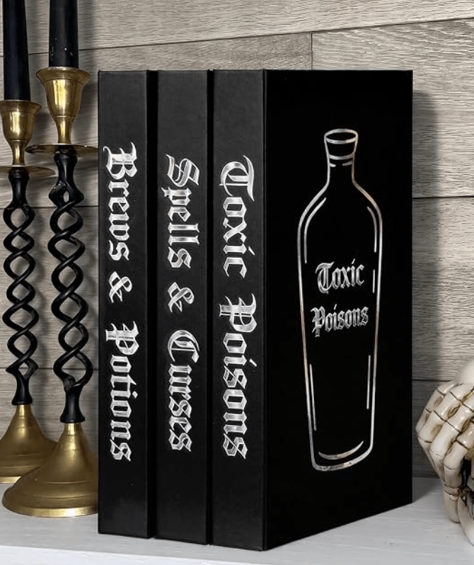 Three decorative black hardcover books standing upright, featuring metallic silver gothic lettering on the spines reading 'Brews & Potions', 'Spells & Curses', and 'Toxic Poisons' with a potion bottle illustration on the cover.